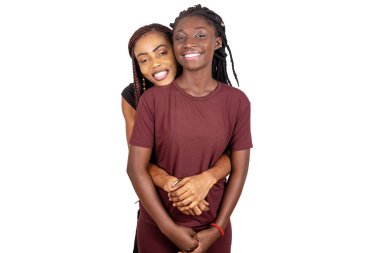 Beyaz arka planda duran ve kameraya gülümseyen iki genç kız kardeş..