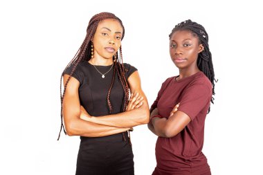 Beyaz arka planda izole edilmiş iki genç kadın kamera kollarının çaprazlanmasını izliyor..