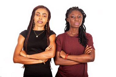 İki güzel kız kardeş ayakta ve kollarını kavuşturup ileriye bakıyorlar ve gülümsüyorlar.