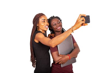 Beyaz arka planda duran iki güzel öğrenci gülümserken cep telefonu kullanarak fotoğrafçıya gidiyorlar..