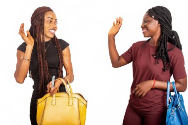 İki güzel genç kız öğrenci el çantalarıyla durup gülümserken birbirlerini selamlıyorlar.