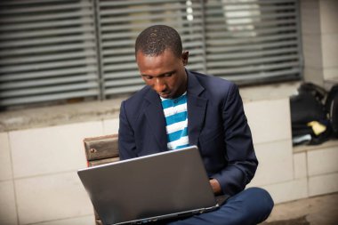 Yakışıklı, genç ve mutlu bir iş adamının görüntüsü. Sokakta bir bankta oturuyor ve dizüstü bilgisayarla çalışıyor.