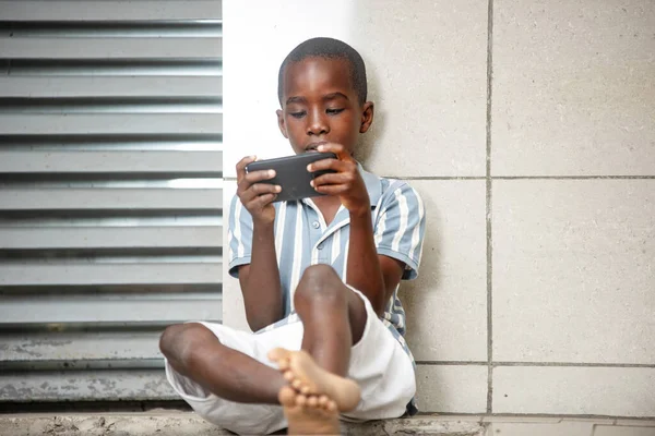 かわいい男の子が屋外の携帯電話でゲームをして座って笑って — ストック写真