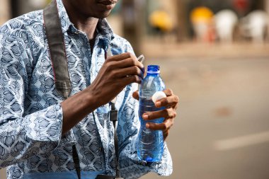 Güzel genç bir turist sokakta duruyor ve plastik şişede maden suyu içiyor.