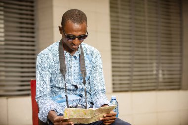 Yabancı turistler dışarıda oturuyor güneş gözlüğü takıyor ve gülümserken harita okuyorlar.