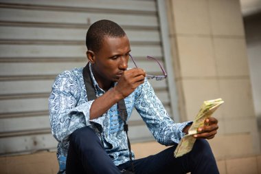 Genç turist merdivenlerde geleneksel kıyafetleriyle oturmuş gözlüklerle coğrafi haritaya bakıyor..