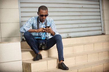 Siyah gözlüklü genç turist cep telefonuna bakıyor..