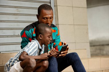 Yakışıklı, genç bir baba oğluyla oturuyor. Babası sokakta gülümserken oğluna görüntüler gösteriyor.