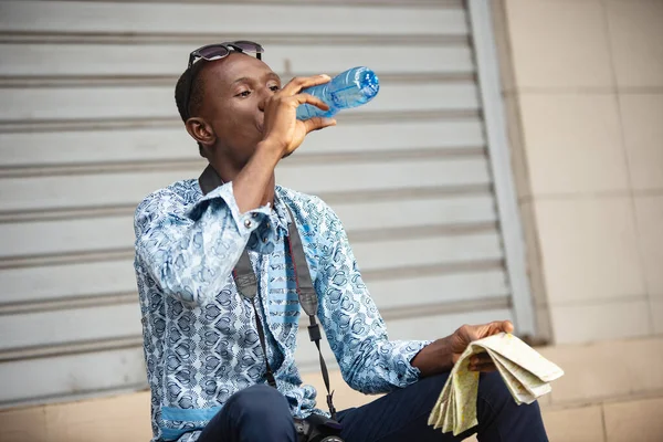 Молодой Фотограф Сидящий Снаружи Пьющий Воду Пластиковой Бутылке Держащий Карту — стоковое фото