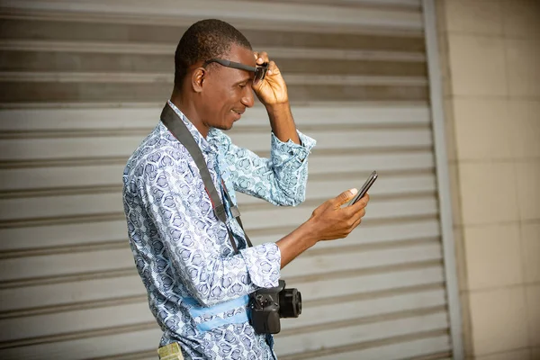 Bonito Jovem Fotógrafo Africano Livre Usando Telefone Celular Enquanto Sorri — Fotografia de Stock