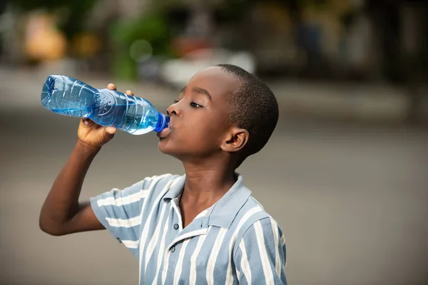 道端に立ってペットボトルの水を飲んでいる美しい男の子 — ストック写真
