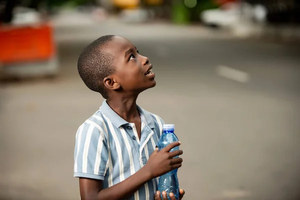 幸せな小さなアフリカの少年がペットボトルを持って横に立って — ストック写真