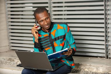 İş adamı bir klasör tutuyor ve müşteriyle cep telefonu görüşmesi yapıyor, ofisin dışında dizüstü bilgisayarla oturuyor..