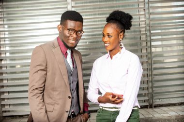 Kahverengi ceketli genç işadamı cep telefonu tutuyor ve dışarıda iş arkadaşlarıyla gülümsüyor.