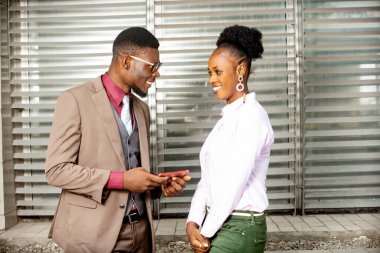 Kahverengi ceketli genç işadamı cep telefonu tutuyor ve dışarıda iş arkadaşlarıyla konuşuyor.