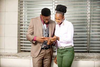 İş adamı ve iş kadını sokakta gülümseyen bir cep telefonu kullanıyor.