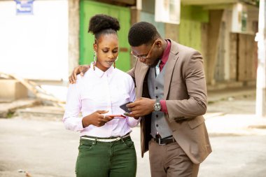 Genç ve güzel bir Afrikalı çift sokakta gülümserken cep telefonu kullanıyor.