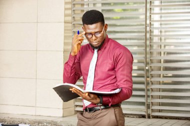 Genç işadamı, Afrikalı elinde kalem olan belgeye bakıyor ve kırmızı bordo bir kimya giydiğini biliyor.