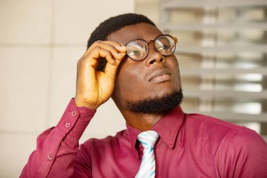 Gözlüklerini tutan genç bir işadamının portresi. Kırmızı bir bordo gömlek ve kravat takıyor.