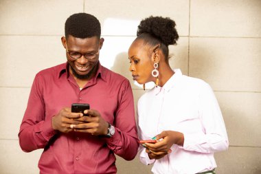 Güzel, meraklı bir kadın, cep telefonuyla mesaj yazarken kocasının omzunun üstünden bakıyor.