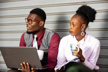 Mutlu iş ortakları oturuyor ve bir dizüstü bilgisayar ve bir fincan kahveyle yan tarafa bakıyor.