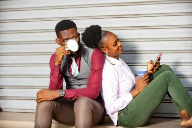 Mutlu, genç Afrikalı çift sırtüstü oturup gülümserken bir fincan kahve içiyorlar.