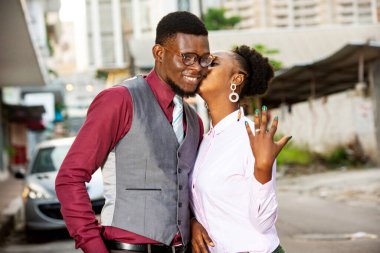 Dışarıda duran genç bir kadın nişanlısını öpüyor ve nişan yüzüğünü gösteriyor..