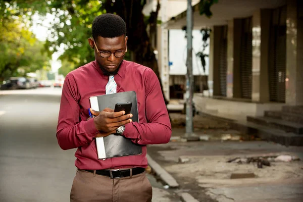 Hombre Negocios Africano Guapo Usando Teléfono Móvil Mientras Sostiene Una —  Fotos de Stock