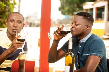 İki genç ortak bir restoranda oturup kırmızı şarap içerek gülümsüyor.