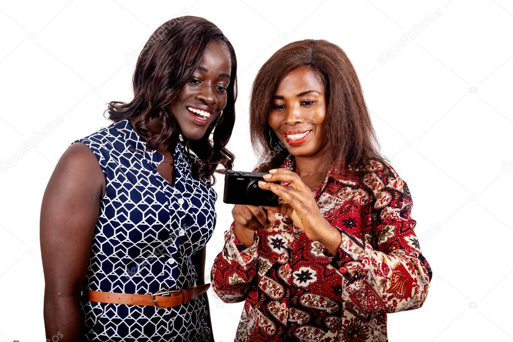 two beautiful young sisters standing and looking at pictures on the camera while smiling, isolated on white background