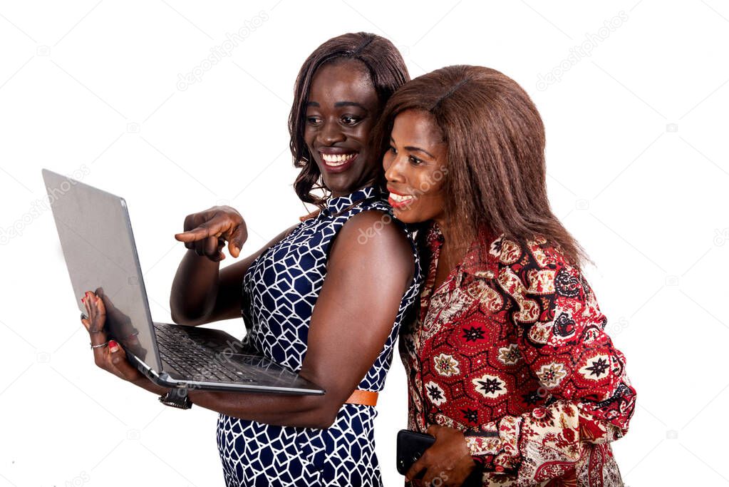 two beautiful african women standing on white background looking at laptop smiling.