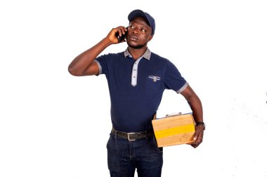 Yakışıklı teslimatçı cep telefonuyla konuşuyor ve elinde bir kartonu tutuyor.