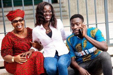 Genç adam dışarıda iletişim kurarken annesi ve kız kardeşi dişlek bir şekilde gülüyor..