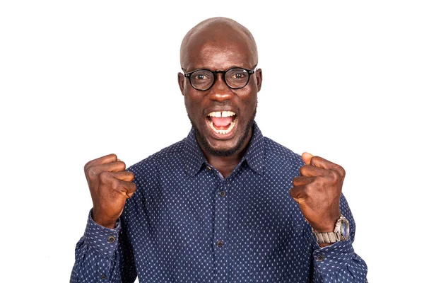 Beyaz arka planda duran yakışıklı genç işadamı mutlu ve heyecanlı bir şekilde kollarını kaldırıp, gülümseyerek ve başarı için bağırarak zafer jesti yapıyor.