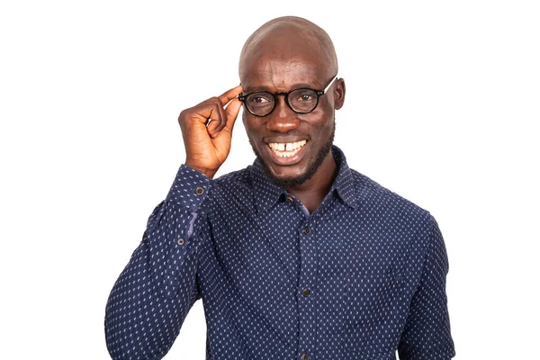 Mutlu gülümseyen genç adam gözlük çerçevesine dokunuyor ve beyaz arka planda izole edilmiş gülümseyen kameraya bakıyor.