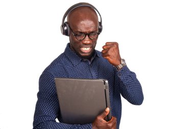 Beyaz arka planda duran yakışıklı iş adamı. Kulaklıklı, dizüstü bilgisayarı olan, eli kapalı gülümseyen.