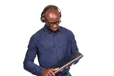 Beyaz arka planda duran, kulaklıklı yakışıklı bir işadamı dizüstü bilgisayara bakıyor.