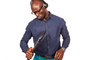 Beyaz arka planda duran, kulaklıklı yakışıklı bir işadamı dizüstü bilgisayara bakıyor.