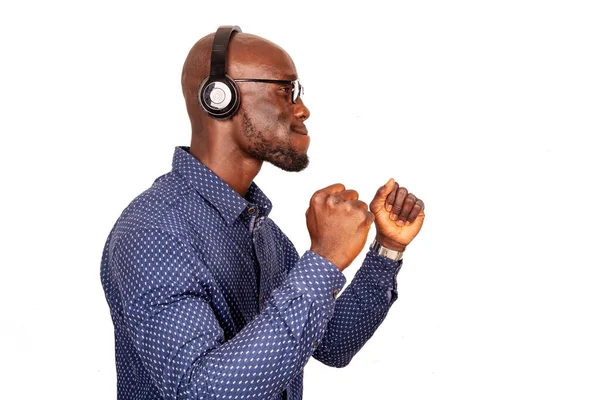 Gözlük takan ve kulaklıkla müzik dinleyen yakışıklı yetişkin bir adam yan bakıyor ve kollarını kaldırıyor.