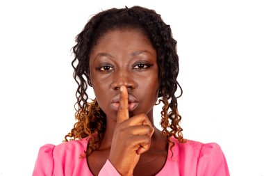 Ciddi, güzel genç bir kadın sessiz bir jest yapıyor. Parmağı dudaklarında ve kameraya bakıyor.