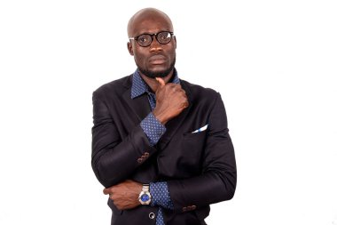 Beyaz arka planda duran takım elbiseli yakışıklı genç bir işadamı kameraya bakıp düşünürken.