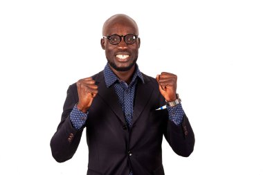 Takım elbiseli yakışıklı genç bir işadamı beyaz arka planda kameraya bakıp kapalı yumruklarla gülümsüyor..