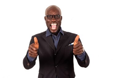 Takım elbiseli yakışıklı genç bir işadamı beyaz arka planda başparmaklarıyla hareket ediyor ve kameraya bakıp neşeyle bağırıyor..