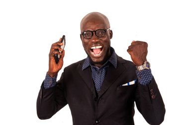 Takım elbiseli yakışıklı genç iş adamı beyaz arka planda cep telefonuyla başarıyı kutluyor..