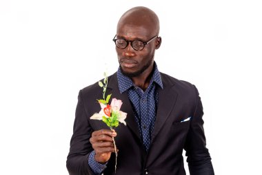 Beyaz arka planda takım elbiseli genç yakışıklı bir adam güzel bir çiçeğe bakıyor..