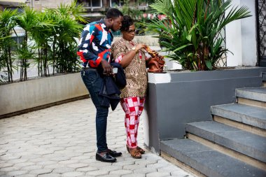 Delikanlı dışarıda karısının çantasından bir şey çıkarışını izliyor.