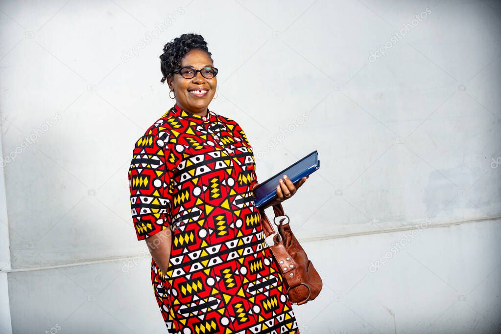 beautiful adult businesswoman wearing glasses and holding a digital tablet and purse and looking at camera smiling