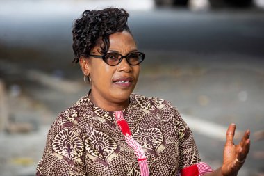 Güzel, olgun bir kadın geleneksel açık hava kıyafetleri içinde oturmuş el hareketleriyle konuşuyor..