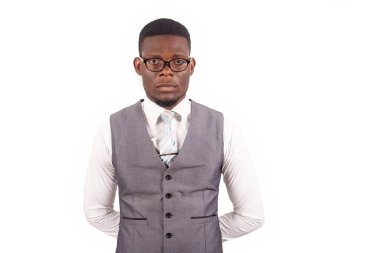 Ciddi, yakışıklı, gözlüklü ve gri takım elbiseli genç işadamı elleri arkada duruyor ve beyaz izole edilmiş arka planda ciddi şekilde ileriye bakıyor.