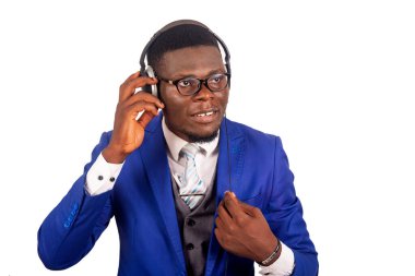 Ceketli genç işadamı beyaz arka planda tek başına durmuş kulaklık kullanarak müzik dinliyor ve gülüyor.